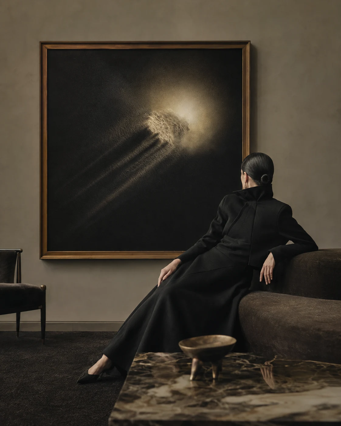 黒い装いの人物が、金色の額に収められた光の抽象画を眺める室内。 Visual 02.